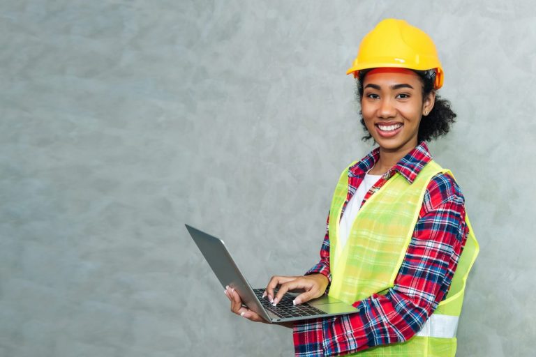 Imagen de mujer sonriente con casco y laptop illustra el blog: "Cómo Ser Supervisor de Almacén"