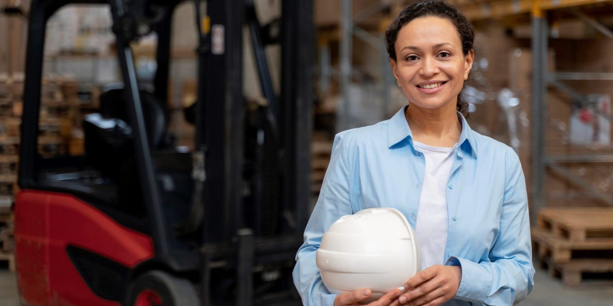 Photo of woman in warehouse with hard hat under her arm illustrates blog: "Career Growth With Warehouse Jobs: What You Need To Know"