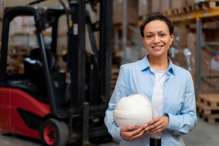 Photo of woman in warehouse with hard hat under her arm illustrates blog: "Career Growth With Warehouse Jobs: What You Need To Know"