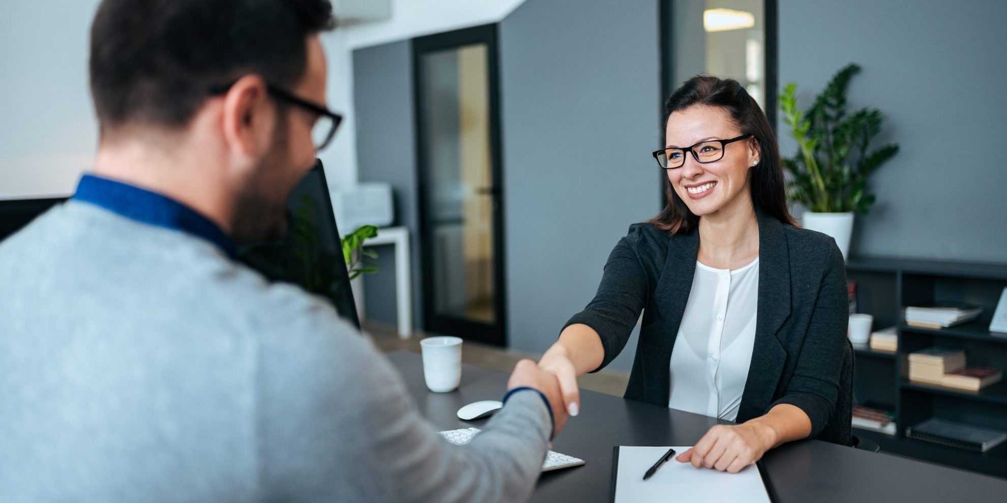 Man and woman shaking hands in office illustrating blog; "How To Prepare for an Office Job Interview? "